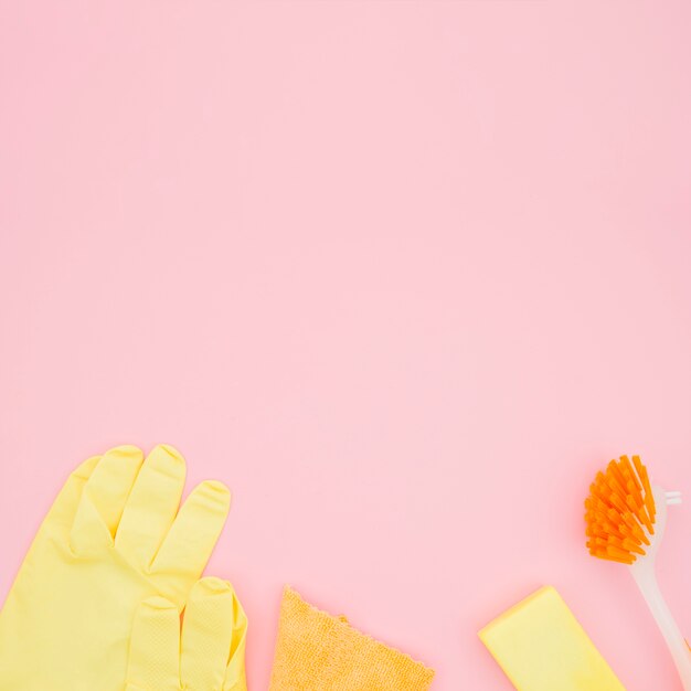 Una vista dall&#39;alto dei guanti; spazzola; spugna e bottiglia su sfondo rosa