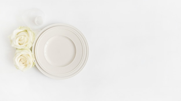 Una vista dall&#39;alto del nastro arrotolato; rose e piatti su sfondo bianco