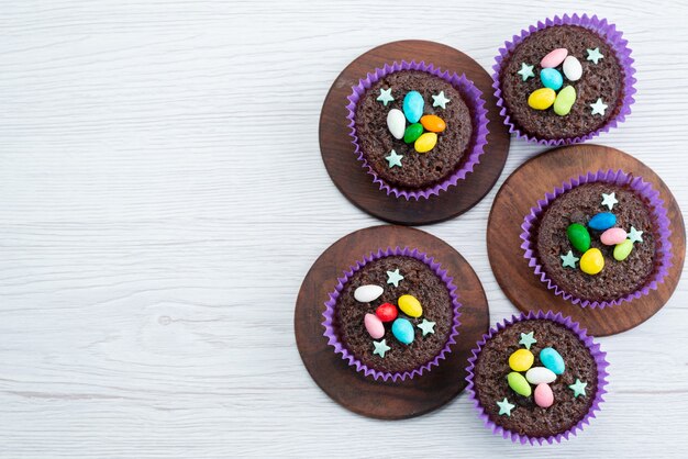 Una vista dall'alto deliziosi brownies all'interno di forme viola con caramelle colorate su bianco, caramelle color caramelle