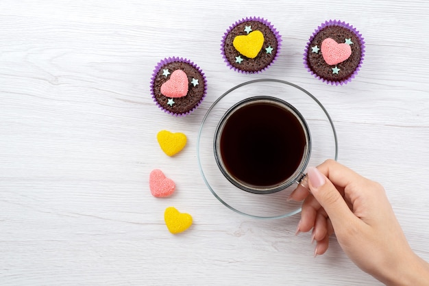 Una vista dall'alto deliziosi brownies all'interno di forme viola insieme a una tazza di tè su dolci bianchi color caramella