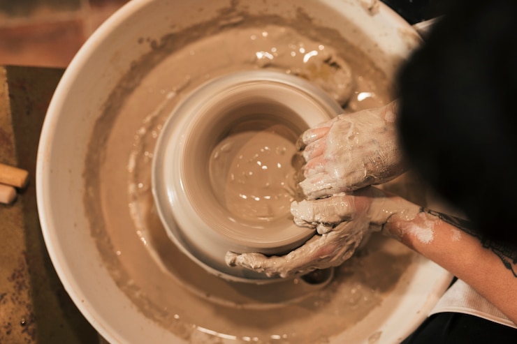 Foto gratuito una vista dall&#39;alto della mano del vasaio femminile creando un vaso di terracotta sulla ruota di ceramica