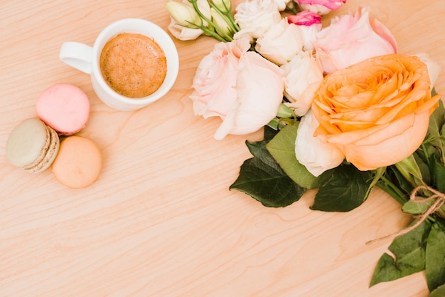 Una vista dall&#39;alto della tazza di caffè; amaretti e bouquet di fiori su fondo in legno