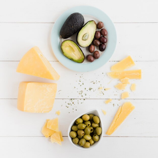 Una vista dall&#39;alto di avocado; pezzo di olive e formaggio sul tavolo bianco