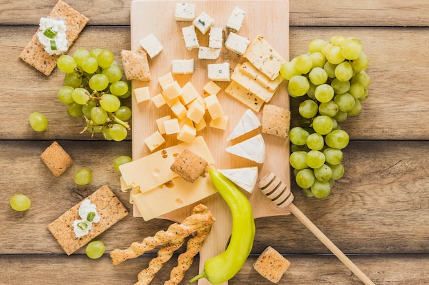Una vista dall&#39;alto di blocchi di formaggio, uva, pane croccante con crema di formaggio; peperoncino verde sul tavolo di legno