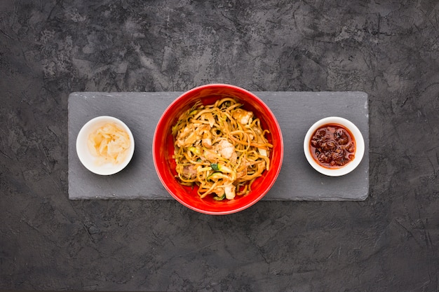Una vista dall&#39;alto di deliziosi noodles in una ciotola con salsa e zenzero marinato su pietra ardesia nera