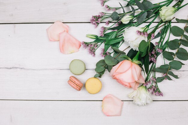 Una vista dall&#39;alto di rosa; limonium ed eustoma bouquet di fiori con amaretti sullo scrittorio di legno bianco