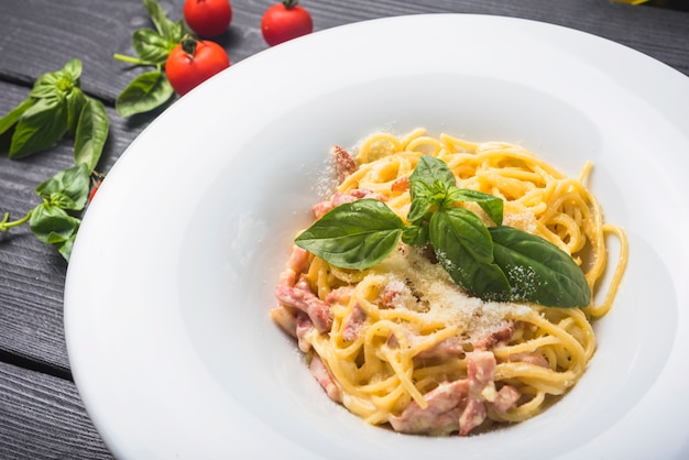 Una vista dall&#39;alto di spaghetti con condimenti di foglia e formaggio basilico sul piatto bianco