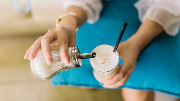 Una vista dall&#39;alto di una donna aggiungendo zucchero nel bicchiere di latte macchiato