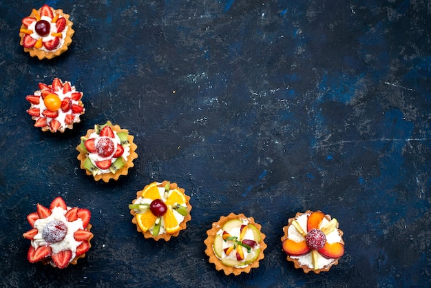 Una vista dall'alto diversi piccoli dolci con crema e frutta fresca a fette sul biscotto torta di frutta sfondo blu