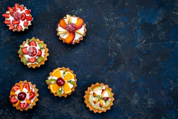 Una vista dall'alto diversi piccoli dolci con crema e frutta fresca a fette sullo sfondo blu torta di frutta biscotto zucchero del tè