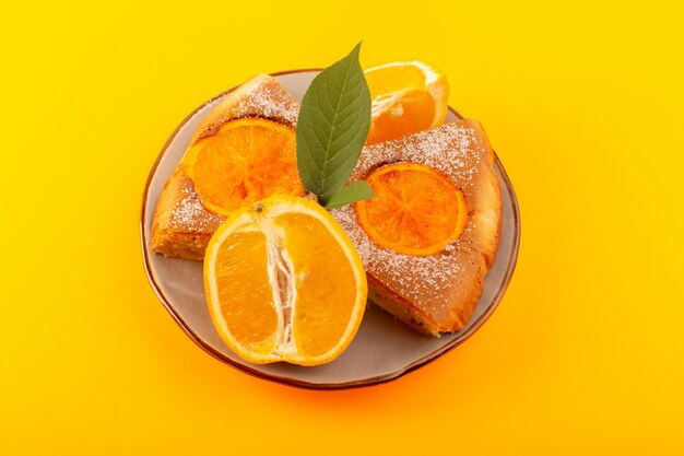 Una vista dall'alto dolce all'arancia dolce deliziose fette di torta insieme all'arancia a fette all'interno del piatto rotondo sullo sfondo giallo zucchero dolce biscotto