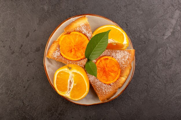 Una vista dall'alto dolce torta all'arancia dolce deliziose fette di torta con fette d'arancia all'interno del piatto rotondo sullo sfondo grigio biscotto zucchero dolce