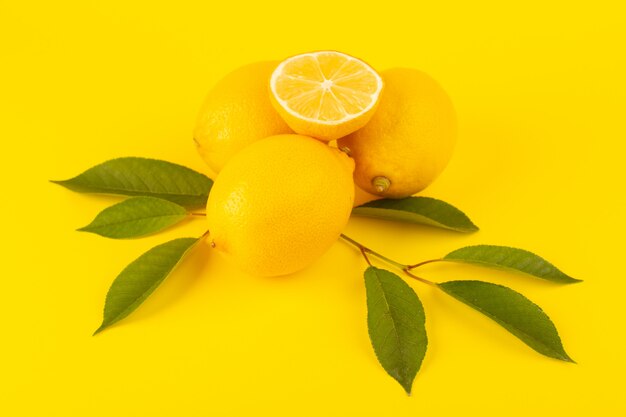 Una vista dall'alto giallo fresco limoni freschi maturi interi e affettati insieme con foglie verdi frutti isolati su sfondo giallo colore di agrumi