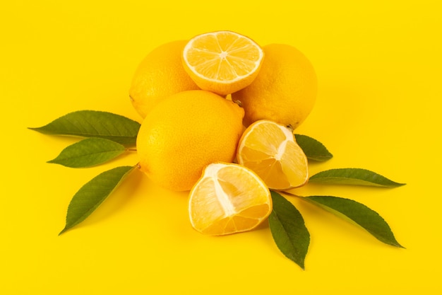 Una vista dall'alto giallo fresco limoni freschi maturi interi e affettati insieme con foglie verdi frutti isolati su sfondo giallo colore di agrumi