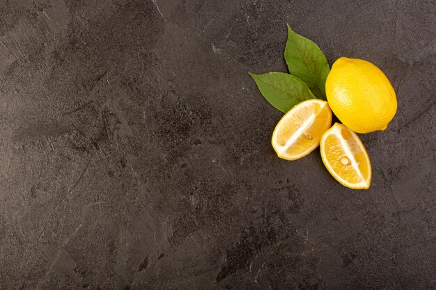 Una vista dall'alto giallo limoni freschi morbido e succoso intero e affettato con foglie verdi su sfondo scuro frutti di colore di agrumi