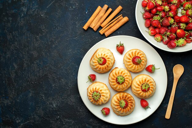 Una vista dall'alto gustosi biscotti con fragole rosse all'interno del piatto bianco sul biscotto scuro dello scrittorio