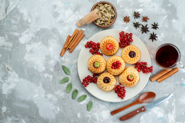 Una vista dall'alto gustosissime torte all'interno del piatto bianco con ciliegie e fragole insieme a cannella e tè sulla torta di frutta leggera