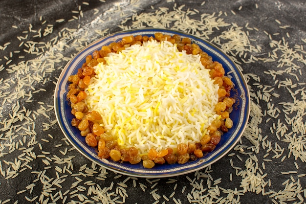 Una vista dall'alto gustoso pilaf con olio e uvetta essiccata all'interno del piatto con riso crudo sulla superficie scura