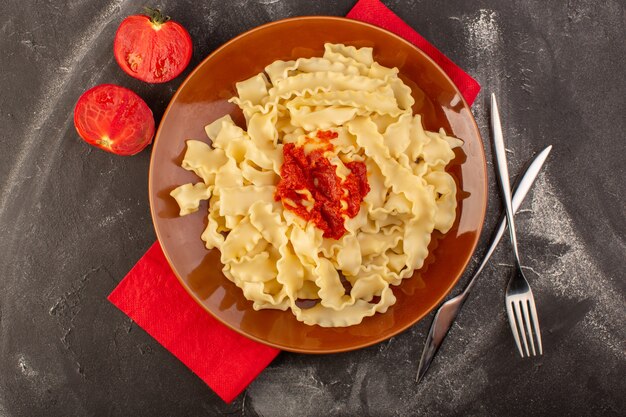 Una vista dall'alto ha cucinato la pasta italiana con le posate ei pomodori della salsa di pomodoro all'interno del piatto