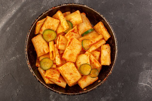 Una vista dall'alto ha cucinato la pasta italiana con salsa di pomodoro e cetriolo all'interno della padella sulla pasta italiana del pasto dell'alimento della tavola scura