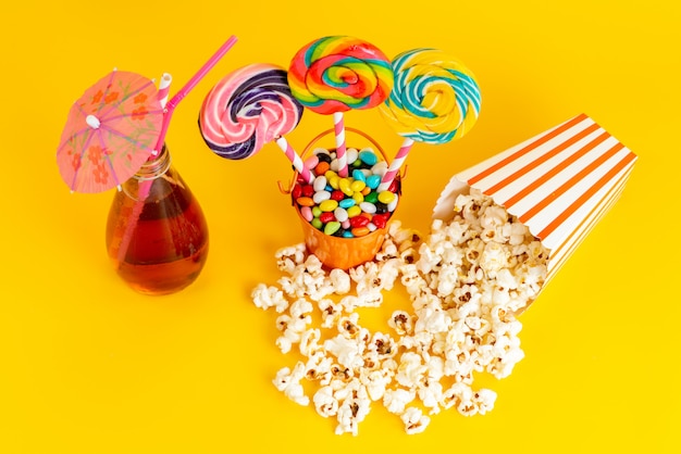Una vista dall'alto lecca-lecca e popcorn con cocktail e caramelle multicolori sullo sfondo giallo bere confettura di zucchero