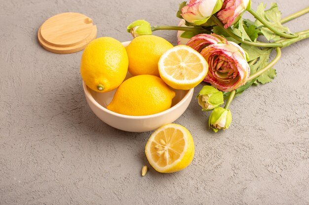 Una vista dall'alto limoni freschi acidi maturi interi con caramelle colorate fiori secchi agrumi gialli tropicali vitamina giallo sulla scrivania crema