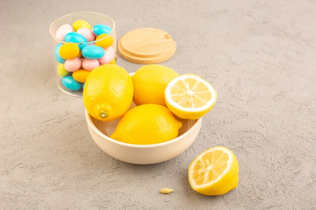 Una vista dall'alto limoni freschi aspro maturo intero morbido con caramelle colorate colorate agrume tropicale vitamina giallo sulla scrivania crema