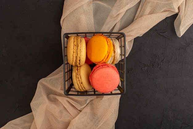 Una vista dall'alto macarons francesi colorati deliziosi e cotti al forno all'interno del canestro sullo zucchero biscotto biscotto torta tavolo scuro