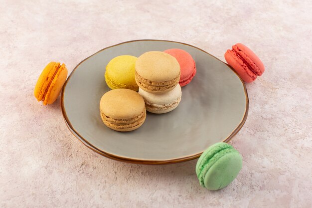 Una vista dall'alto macarons francesi colorati gustosi e deliziosi all'interno del piatto sullo zucchero torta rosa da scrivania dolce