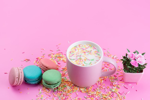 Una vista dall'alto macarons francesi insieme a particelle di caramelle colorate tutto su rosa, dolce di zucchero del biscotto della torta del pavimento