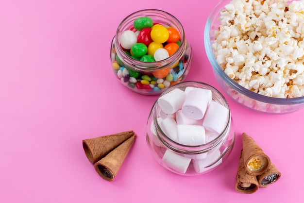 Una vista dall'alto marshmallow e popcorn insieme a caramelle colorate su confettura color zucchero e rosa