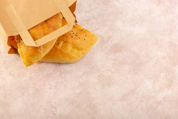 Una vista dall'alto pane cotto caldo gustoso fresco all'interno di pacchetti di carta sul rosa