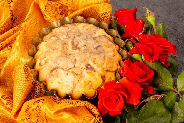 Una vista dall'alto rotonda torta dolce deliziosa e squisita torta al cioccolato all'interno della tortiera insieme a rose rosse isolate su sfondo grigio