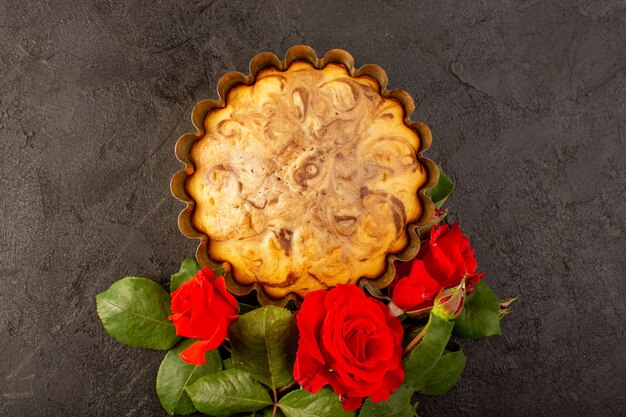 Una vista dall'alto rotonda torta dolce deliziosa e squisita torta al cioccolato all'interno della tortiera insieme a rose rosse isolate su sfondo grigio