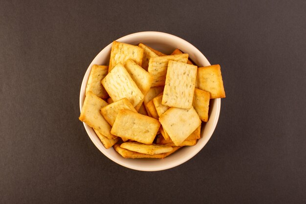 Una vista dall'alto salato patatine gustose crackers formaggio all'interno del piatto bianco su sfondo scuro spuntino sale cibo croccante