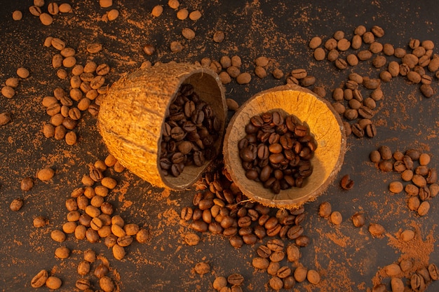 Una vista dall'alto semi di caffè marrone all'interno e all'esterno di gusci di noce di cocco sul granulo marrone del chicco del seme di caffè dello scrittorio