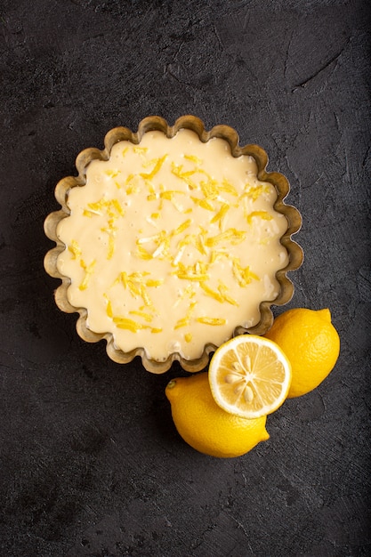 Una vista dall'alto torta al limone aspro delizioso dolce da forno esotico dolce con limoni freschi sulla scrivania scura