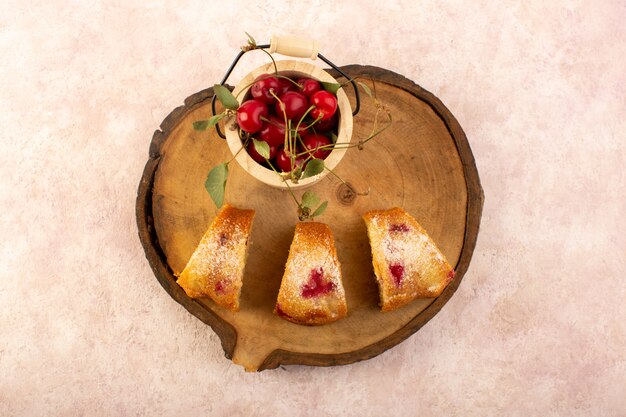 Una vista dall'alto torta di frutta al forno deliziosa affettata con ciliegie rosse all'interno e zucchero in polvere sulla scrivania in legno con ciliegie fresche sul rosa