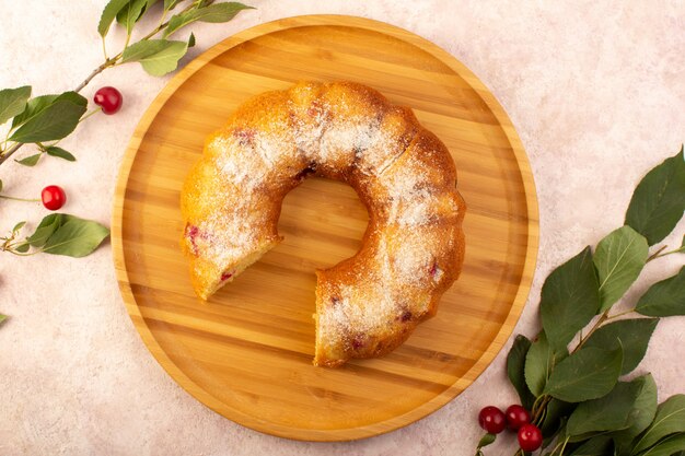 Una vista dall'alto torta di frutta al forno deliziosa affettata con ciliegie rosse all'interno e zucchero in polvere sullo scrittorio rotondo di legno sul colore rosa