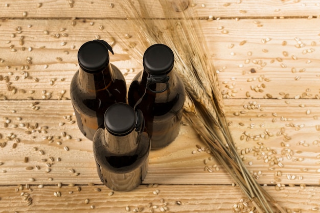 Una vista di alto angolo di tre bottiglie alcoliche e spighe di grano su superficie di legno