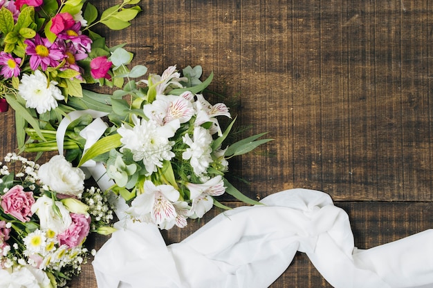 Una vista elevata del bouquet di fiori con sciarpa bianca sul tavolo di legno