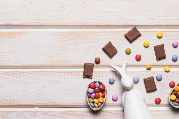 Una vista elevata del coniglio bianco con caramelle di gemme e pezzi di cioccolato su tavola di legno