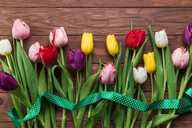 Una vista elevata del nastro verde sopra i tulipani colorati sulla plancia con texture in legno