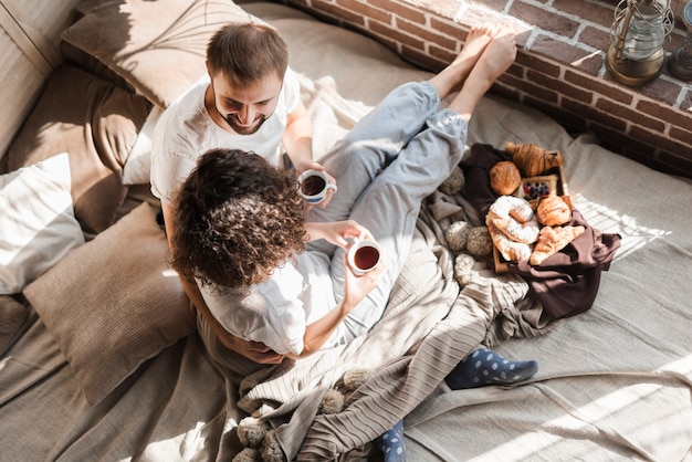 Una vista elevata delle coppie che si siedono sul letto che tiene tazza di caffè