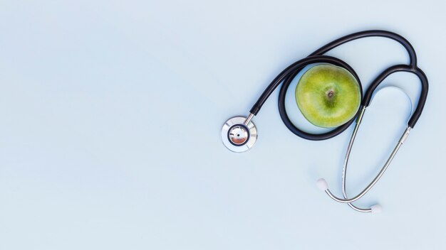 Una vista elevata dello stetoscopio intorno alla mela verde sopra fondo blu