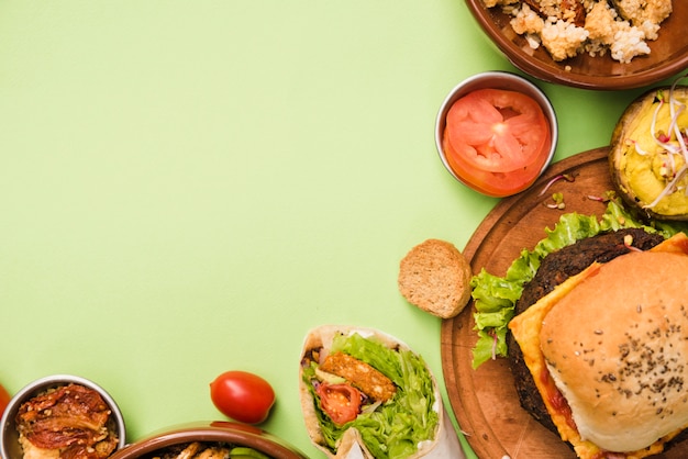 Una vista elevata di burrito avvolgere; insalata e hamburger su sfondo verde