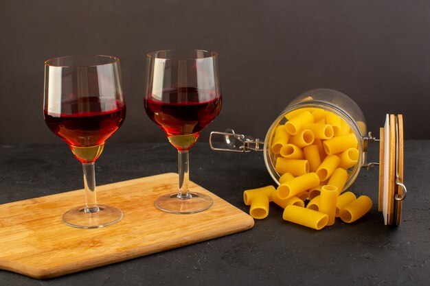 Una vista frontale bicchieri di vino sullo scrittorio di legno marrone lungo pasta italiana cruda su oscurità