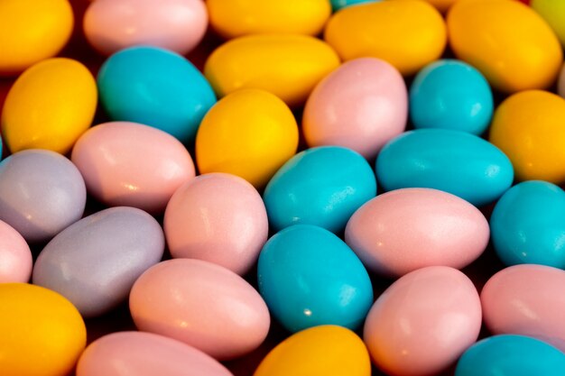 Una vista frontale caramelle multicolori bon-bons dolce gustoso sui biscotti rossi di dolcezza della pasticceria del fondo scuro del tessuto
