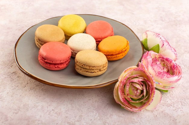 Una vista frontale colorati macarons francesi con rose sul colore rosa biscotto torta scrivania