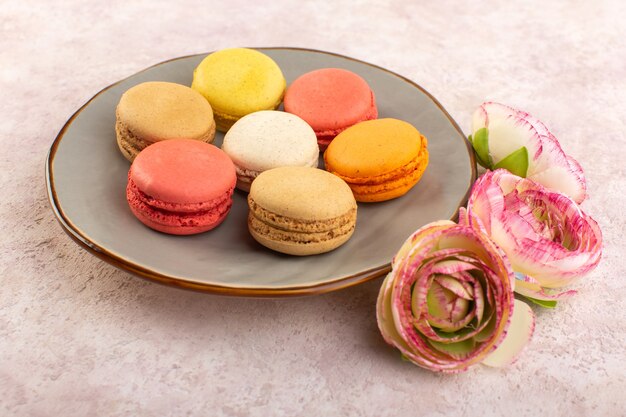 Una vista frontale colorati macarons francesi con rose sul colore rosa biscotto torta scrivania